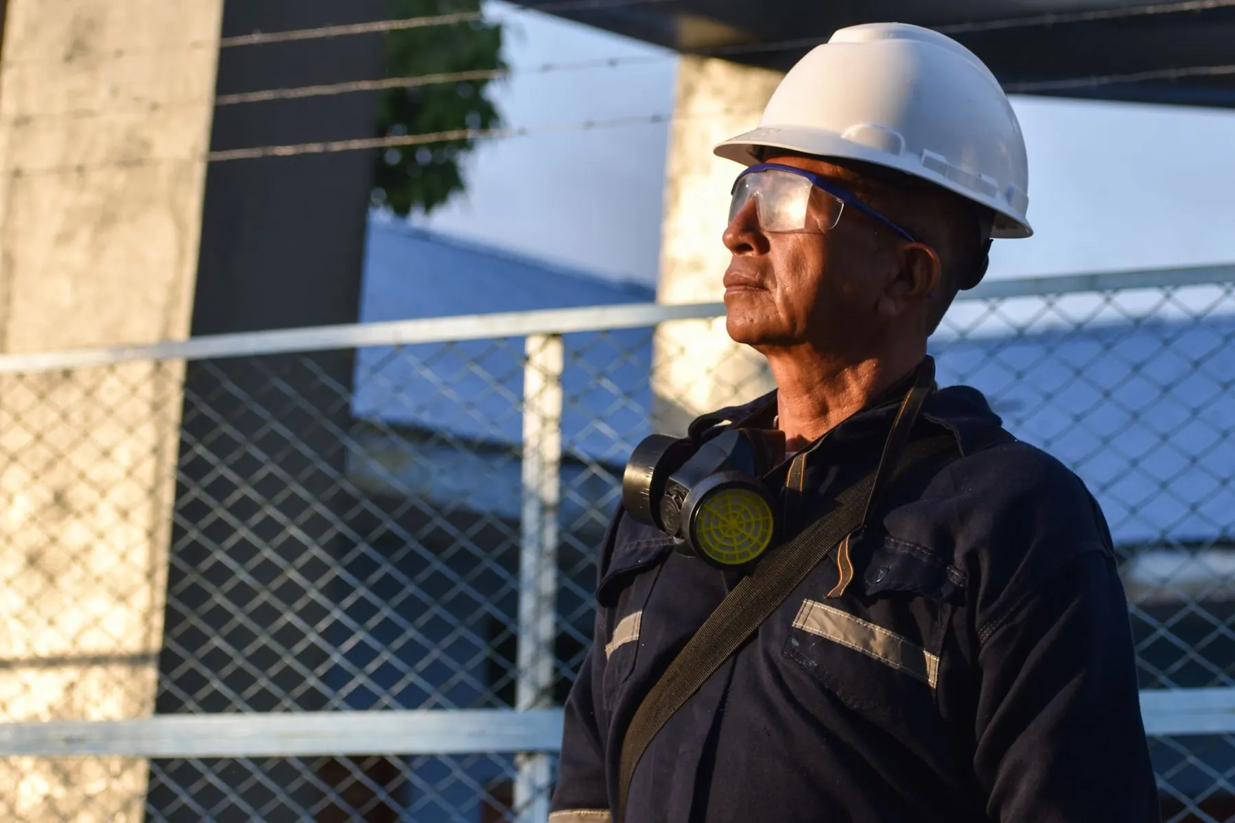 Trabalhador de capacete e óculos de proteção, com respirador no pescoço, olhando ao longe