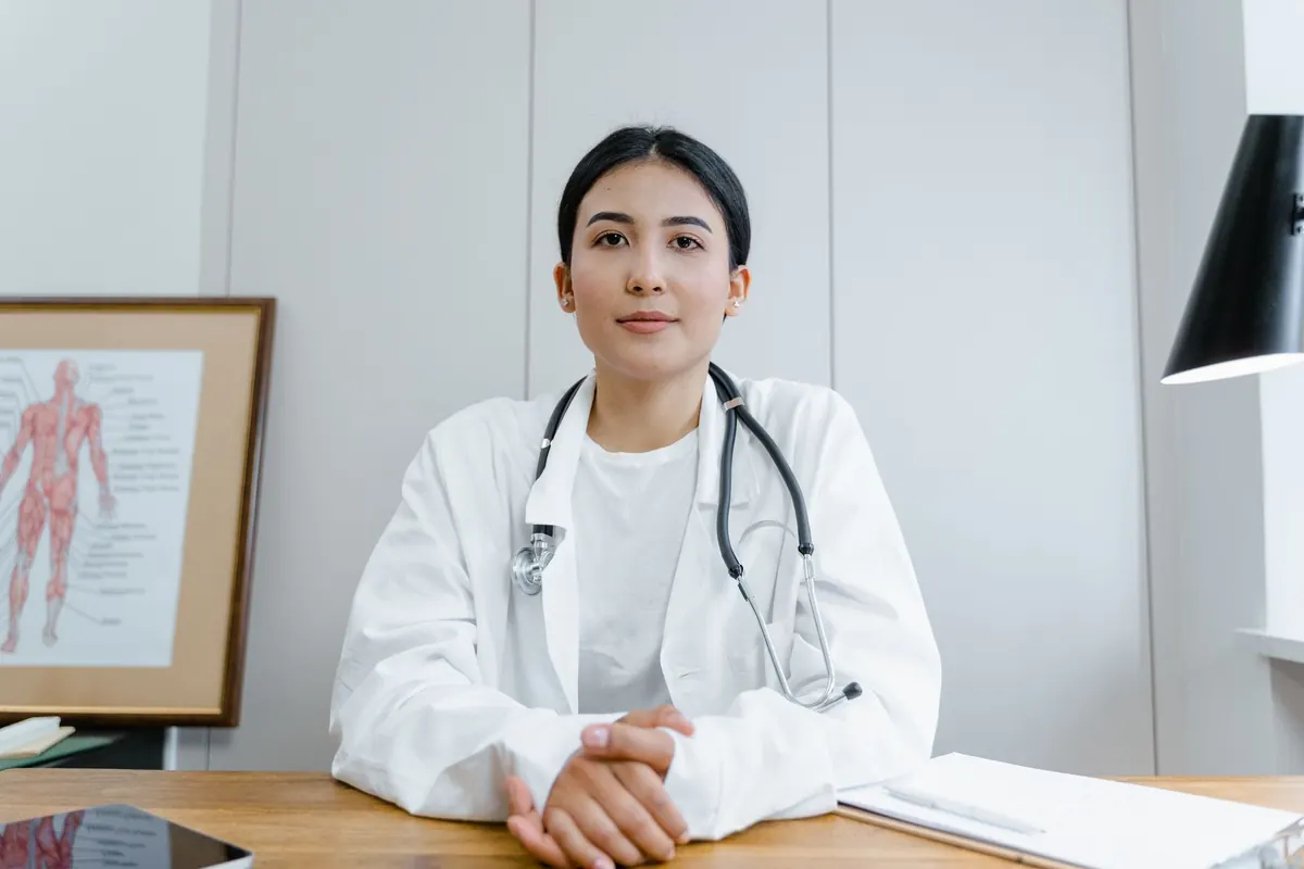 Médica sentada à mesa do consultório, olhando para a câmera